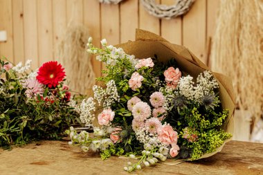 Çiçekçinin ahşap masasına yerleştirilmiş pembe ve beyaz çiçeklerle dolu bir buket teslim edilmeye ya da toplanmaya hazır, Anneler Günü.