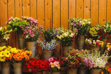 Çiçekçinin ahşap raflarında metal kovalarda sergilenen çeşitli taze çiçeklerden oluşan renkli buketler canlı ve davetkar bir atmosfer yaratıyor, Anneler Günü.