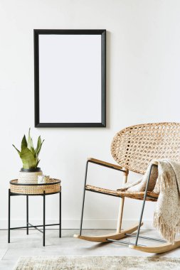 Oturma odasının iç dekorasyonu, tasarım rattan koltuğu, siyah poster çerçevesi, sehpa, bitki, dekorasyon, beyaz duvar ve kişisel aksesuarlar. Şablon.