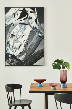 Ahşap masa, siyah sandalyeler, deisgn cam tepsi, vazoda tropikal yaprak, duvarda soyut resimler ve zarif aksesuarlar. Modern ev dekorasyonu. Şablon.