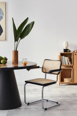 Yemek odasının tasarım masası, modern sandalyeler, dekorasyon, vazoda tropikal yaprak, meyve, kitaplık, soyut tasarım tabloları ve ev dekorunda zarif aksesuarlarla iç mimarisi..