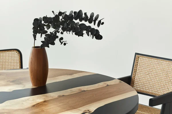 Stylish composition on the design table with elegan black eucalyptus flowers in timber vase. Modern dining room interior. Template.