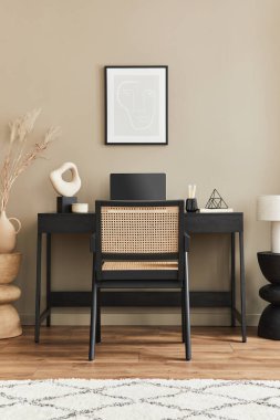 Ev ofisinin içinde siyah ahşap masa, sandalye, vazoda kurutulmuş çiçek, dizüstü bilgisayar, poster çerçevesi, bir fincan kahve, saat ve şık ofis aksesuarları olan şık bir kompozisyonu. Şablon.