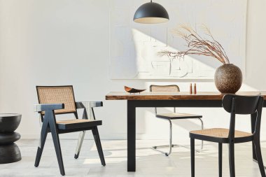 Ahşap masa, dizayn sandalyeleri, vazoda kurumuş çiçekler, siyah kolye lambası, duvarda resim resimleri ve zarif kişisel aksesuarlarla yemek odasının minimalist kompozisyonu. Şablon.