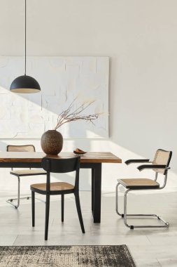 Ahşap masa, dizayn sandalyeleri, vazoda kurumuş çiçekler, siyah kolye lambası, duvarda resim resimleri ve zarif kişisel aksesuarlarla yemek odasının minimalist kompozisyonu. Şablon.