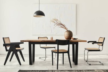 Ahşap masa, dizayn sandalyeleri, vazoda kurumuş çiçekler, siyah kolye lambası, duvarda resim resimleri ve zarif kişisel aksesuarlarla yemek odasının minimalist kompozisyonu. Şablon.