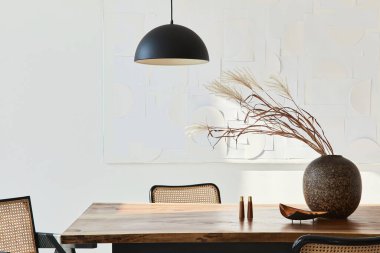 Ahşap masa, dizayn sandalyeleri, vazoda kurumuş çiçekler, siyah kolye lambası, duvarda resim resimleri ve zarif kişisel aksesuarlarla yemek odasının minimalist kompozisyonu. Şablon.
