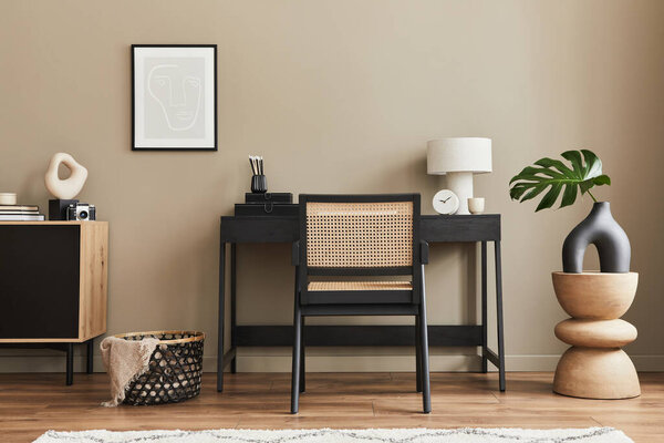 Modern interior design of home office space with stylish chair, desk, commode, black mock up poster frame, lapatop, book, office supply and elegant presonal accessories in home decor. Template.