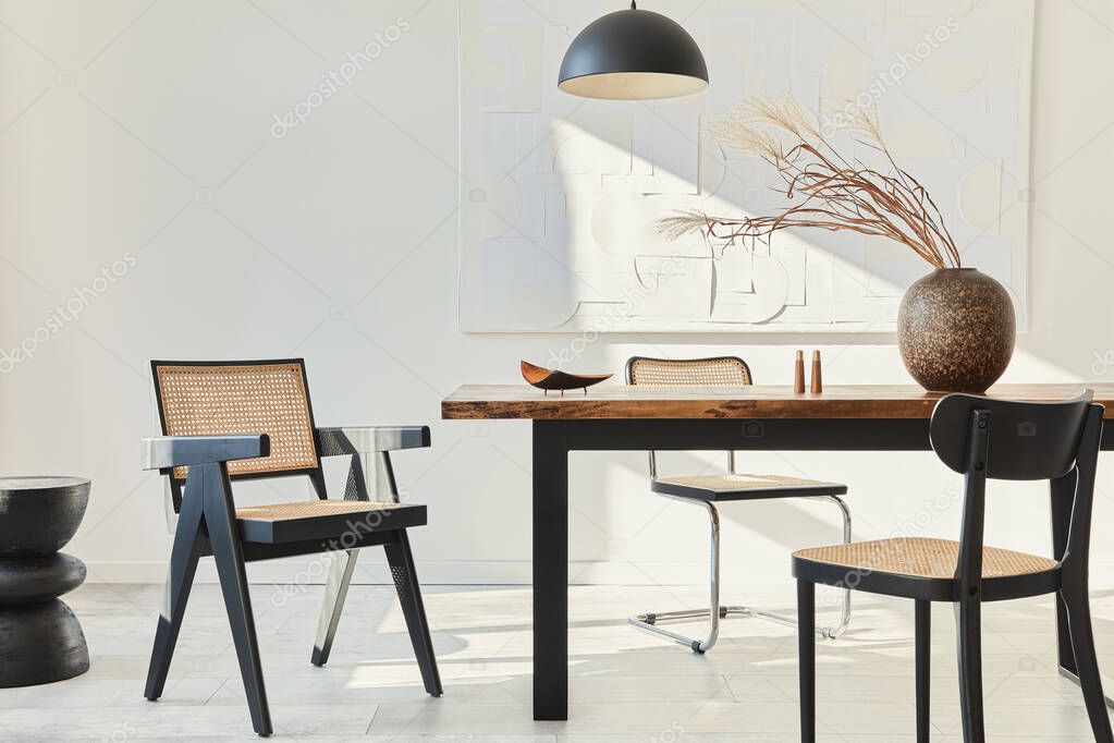 Minimalist composition of dining room interior with wooden table, design chairs, dried flowers in a vase, black pendant lamp, art paintings on the wall and elegant personal accessories. Template.