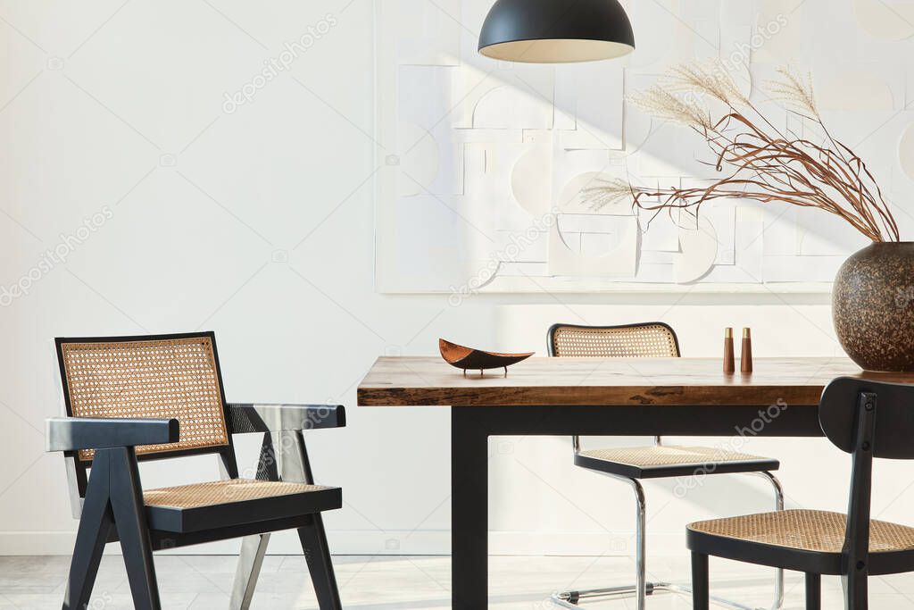 Minimalist composition of dining room interior with wooden table, design chairs, dried flowers in a vase, black pendant lamp, art paintings on the wall and elegant personal accessories. Template.