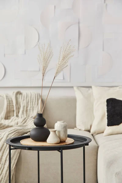 Stylish composition at fancy interior with wooden coffee table, dried flowers in vase, pillow, blanket, art painitngs and book in modern home decor. Details. Template.