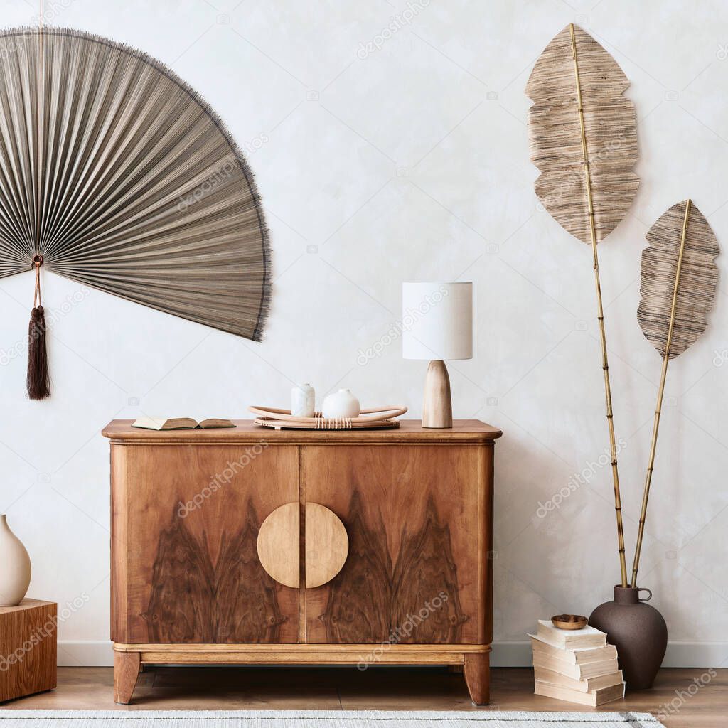 Japandi concept of living room interior with design wooden commode, table lamp, tropical dried leaf in vase, cubes, decoration, japanese fan and elegant personal accessories in home decor. Template.