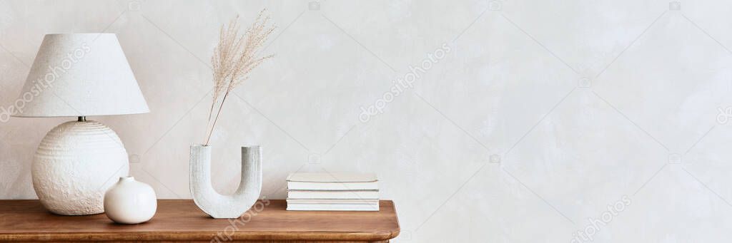 Minimalist composition of living room with wooden commode, table lamp, dried flower in vase, book, decoration and elegant personal accessories in stylish home decor. Template. Copy space.