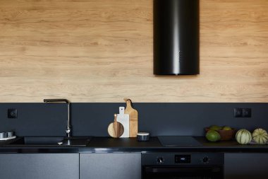 Modern küçük mutfak içinin şık bir kompozisyonu. Siyah mutfak çalışma alanı, siyah ve açık renk ahşap mutfak aksesuarları. Tahta panel yaratıcı duvarlar. Minimalist erkeksi kavram. Şablon.