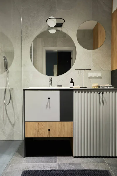 Stylish composition of modern bathroom interior. Modern designed shower, mixed wooden commode, mirror and personal accesories. Grey creative walls with black and light wooden panels. Minimalistic masculine concept. Template.