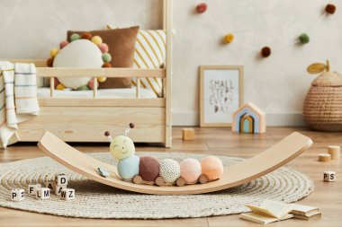 Creative composition of cozy scandinavian child's room interior with plush caterpillar on the balance board, wooden toys and textile decorations. Neutral wall, carpet on the floor. Details. Template. clipart