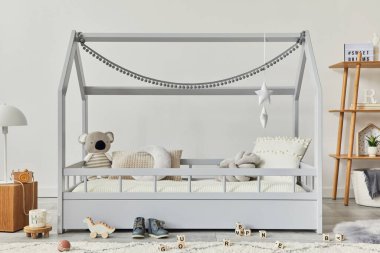 Şık İskandinav çocuk odası, yaratıcı ahşap yatak, tahta küp, lamba, ahşap raf, peluş ve ahşap oyuncaklar ve asılı tekstil süslemeleri. Gri duvarlar. Şablon.