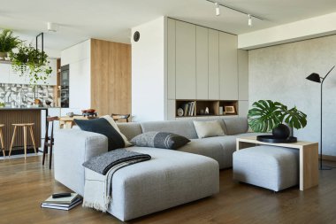Gri kanepe, puf ve kişisel aksesuarları olan şık bir oturma odası tasarımı. Yemek odası ve mutfak arka planda. Ahşap panjurlu yaratıcı duvarlar. Minimalist stil bir bitkisel aşk konsepti. 