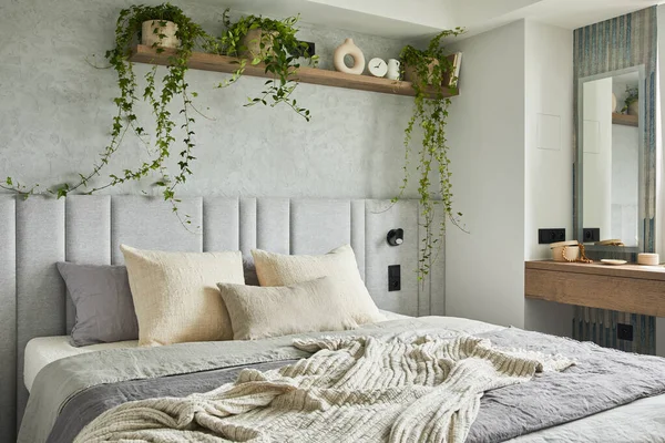 Stylish bedroom interior in modern apartment with small bed, wooden chest, home garden, white bedding, pillows and blanket. Sunny space with grey walls and brown wooden parquet. Template