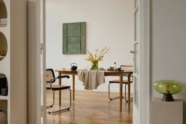 Yeşil duvar sanatı ve bahar çiçekleriyle dolu ılık tonlu yemek salonu. Yumuşak kumaşlar ve basit, modern dekorlarla İskandinav esinlenilmiş iç mekan.