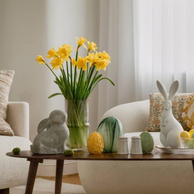 Parlak, modern bir oturma odasındaki sehpanın üzerinde stilize Paskalya dekoru. Tatil, bahar kutlamaları ve neşeli ev dekorasyonu için kullanılıyor.