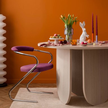 Paskalya kutlamasının parlak iç görüntüsü sandalye ve turuncu duvarlı modern bir masaya serilmiş. Tatil, yaşam tarzı ve ev dekorasyonu için.