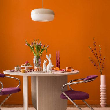 Pastalı canlı Paskalya masası, tavşan heykelcikler, laleler. Turuncu, pembe ve mor arka plan bahar tatili ruhunu yansıtır. Kutlamalar için kullan