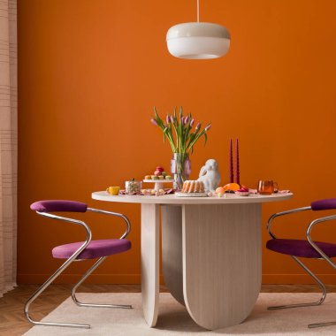 Paskalya için yuvarlak masa seti: pasta, şeker, lale, tavşan heykeli. Sıcak iç mekan, modern sandalyeler. Tatil, dekor, yemek kavramları için kullanılıyor.