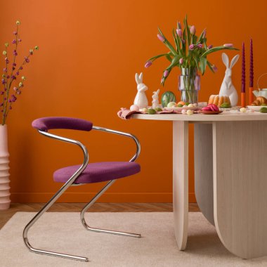 Pastel süslemeler, laleler, seramik tavşanlar ve sıcak turuncu bir duvara dayalı ahşap bir masa..