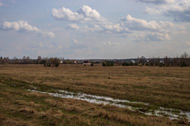 Sahada ilkbahar. Bulutların arasından gün ışığı. Ufukta orman görünüyor. Dramatik bulutlar. Tarlaları ve ağaçları olan manzara.