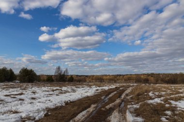 Baharın başında tarladan geçen toprak yol. Buzları çözülmüş bahar manzarası. Bahar buzu. Bulutlar ve alan