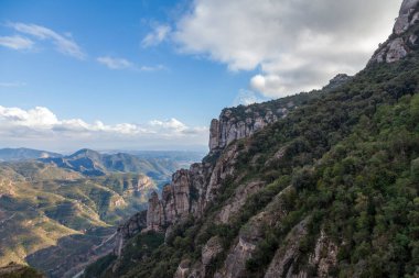 İspanya, Katalonya. Montserrat 'ta kış güneşinin altında bitki örtüsüyle kaplı dağlar. Dağlar, bulutlar, ağaçlar.