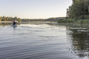 Kano süren bir adam nehirde yüzüyor. Sabahları nehir manzaralı bir manzarayla karşılaşıyorum. Güneşin ışınları ağaçların tepelerine dokunuyor. Yazın sakin bir nehirde sabahın köründe kanoya binmek.