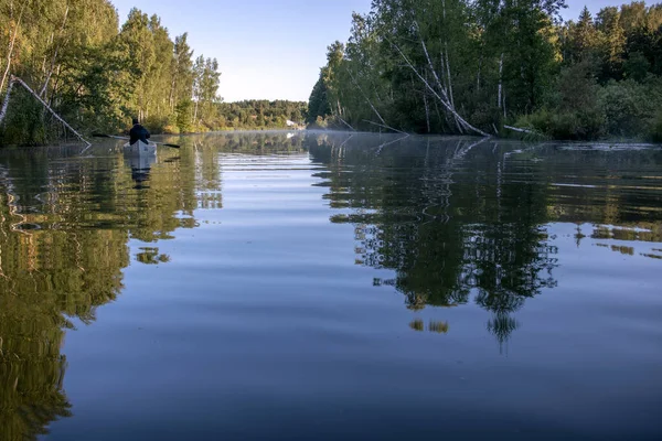 Bir adam gölde bir kanoyla yelken açıyor. Bir teknesi olan resimli sabah manzarası. Nehirde şafak vakti.