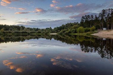 Akşamları nehir kıyısında yaz manzarası. Dramatik bulutlar suya yansıyor. Gün batımından sonra manzarada yoğun renkler.