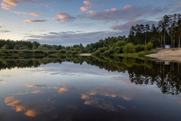 Akşamları nehir kıyısında yaz manzarası. Dramatik bulutlar suya yansıyor. Gün batımından sonra manzarada yoğun renkler.
