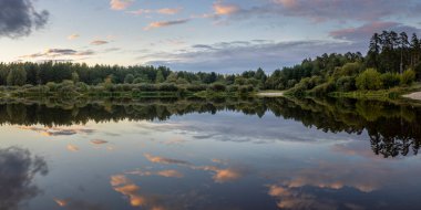 Akşamları nehir kıyısında yaz manzarası. Dramatik bulutlar suya yansıyor. Gün batımından sonra manzarada yoğun renkler.