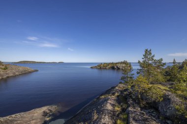 Gölde güneşli bir gün. Suyun içindeki gökyüzünün yansıması. Taş üstünde çam. Kuzeyin doğası..