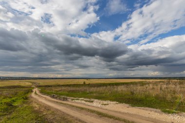 Tarlalardan geçen yol. Yaz tarlasında köy yolu ve mavi gökyüzünde bulutlar..