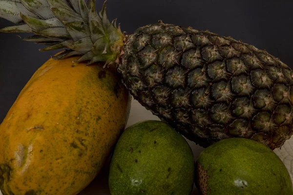 Green growing pineapple with papaya and avocado on dark background