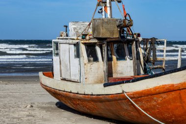 Cabo Polonio, Uruguay sahilinde dinlenen bir balıkçı teknesi. Gemi aşınma izleri gösteriyor, teçhizat ve ipler açık, bulutlu bir gökyüzü ve kıyı rüzgarı altında..