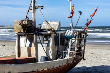 Cabo Polonio, Uruguay sahilinde dinlenen bir balıkçı teknesi. Gemi aşınma izleri gösteriyor, teçhizat ve ipler açık, bulutlu bir gökyüzü ve kıyı rüzgarı altında..