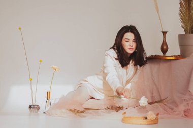 Beyaz ceketli güzel esmer kız ve beyaz tayt içinde beyaz bir gül tutuyor.