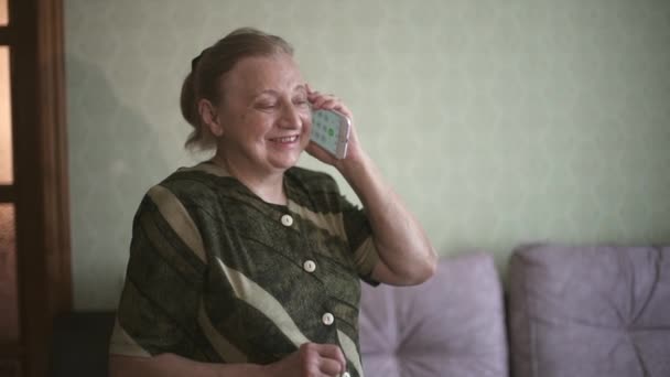 Oma praat emotioneel op haar mobiele telefoon en toont super. Oudere vrouw glimlachte op een smartphone en toonde super. Close-up portret van de oudere vrouw praten aan de telefoon, glimlachen en — Stockvideo