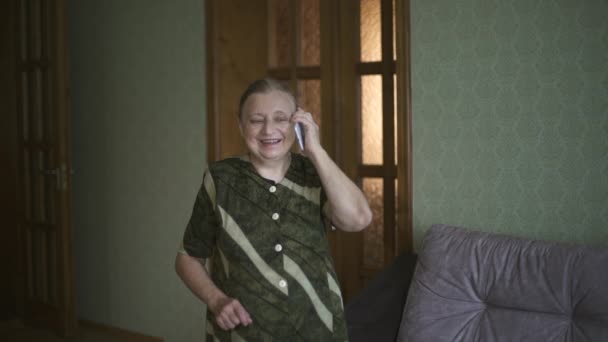 A avó fala emocionalmente no telemóvel e mostra-se super. Mulher idosa sorrindo falando em um smartphone e mostrando super. Close-up retrato da mulher idosa falando ao telefone, sorrindo e — Vídeo de Stock