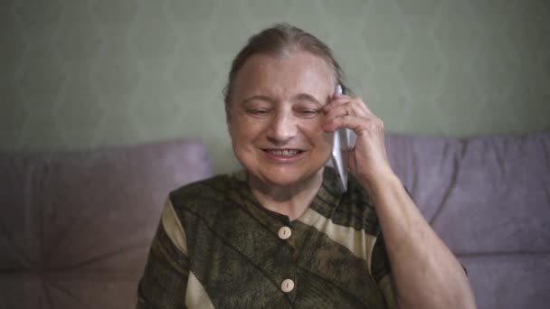 Oma praat emotioneel op haar mobiele telefoon en toont super. Oudere vrouw glimlachte op een smartphone en toonde super. Close-up portret van de oudere vrouw praten aan de telefoon, glimlachen en — Stockvideo