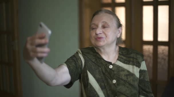 Femme âgée prend un selfie à l'aide de son smartphone. Grand-mère souriante prend quelques selfie-photos sur son téléphone. Vieille dame prend quelques selfies en utilisant son téléphone. — Video