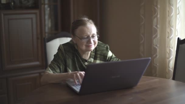 Abuela en los auriculares emocionalmente habla a través de Skype, se quita los auriculares y golpea portátil — Vídeo de stock