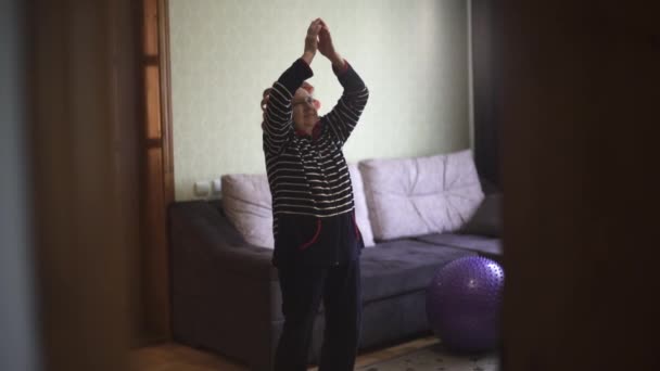Grootmoeder duikt gelukkig op in haar woonkamer. Oude vrouw in krulspelden springt vrolijk op en glimlacht. — Stockvideo