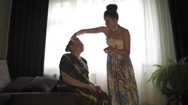 La fille invente le visage de sa grand-mère. Jeune femme se maquille sur le visage d'une vieille femme. — Video